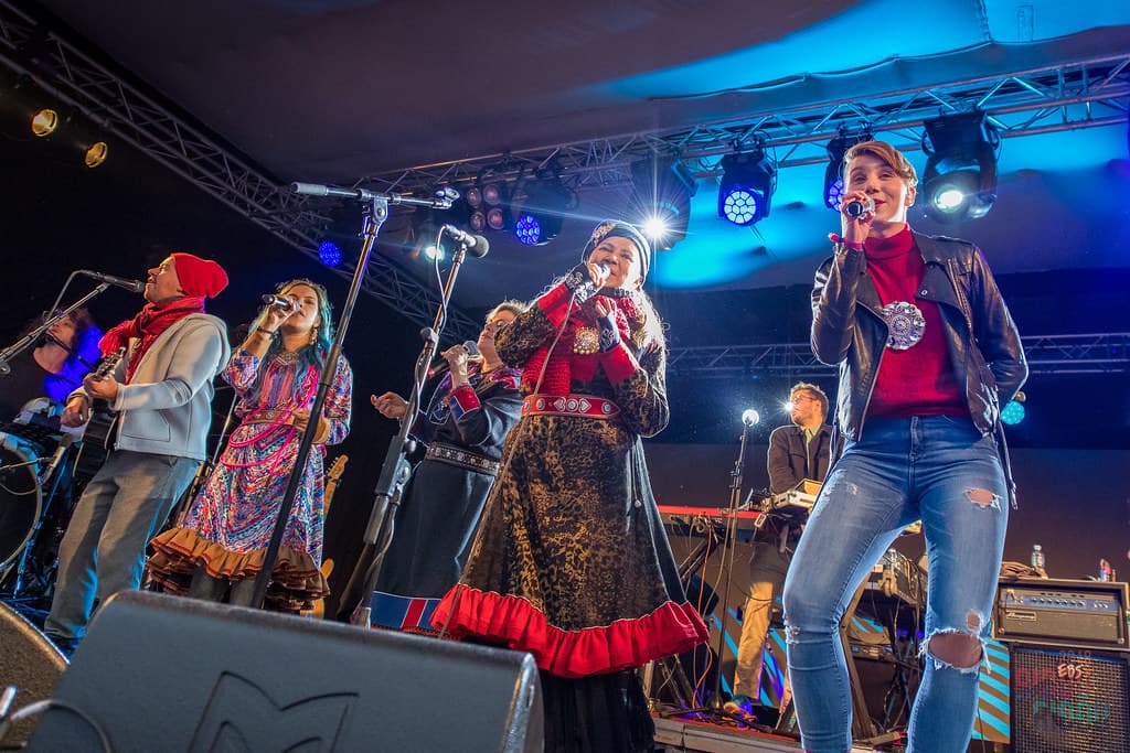 Musicians in Sámi dress and colourful costumes perform on a lit stage at the Riddu Riđđu festival