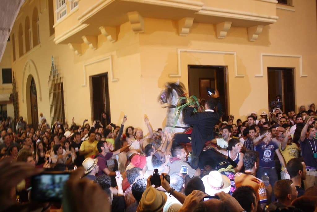 A rider rears his horse above a dense crowd in a square in Ciutadella during the Sant Joan festival at dusk