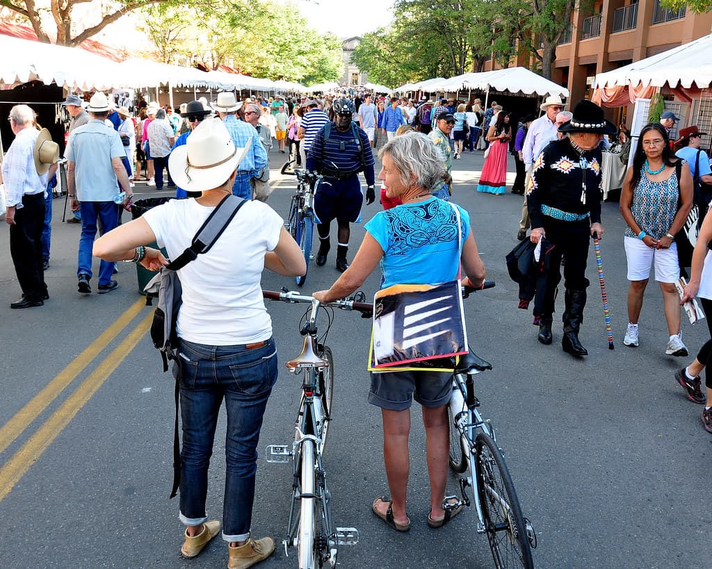 Shoppers and visitors walk between rows of white vendor tents on a street during the Santa Fe Indian Market