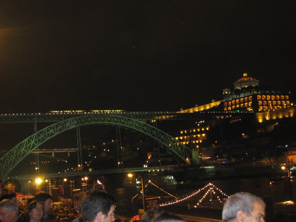 Crowds on Porto's Ribeira waterfront on São João night, with the lit Luís I bridge and Serra do Pilar monastery across the Douro