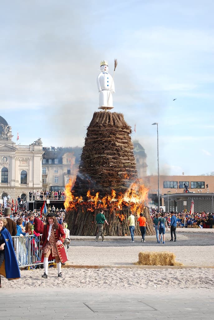 The Böögg, a snowman figure, stands on top of a tall burning bonfire on the Sechseläutenplatz in Zurich