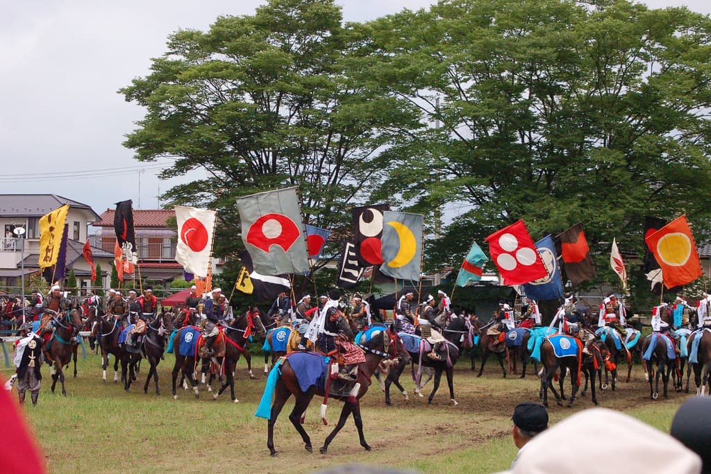 Mounted riders in samurai armour with banners on their backs gallop past spectators during the armoured horse race at Soma Nomaoi