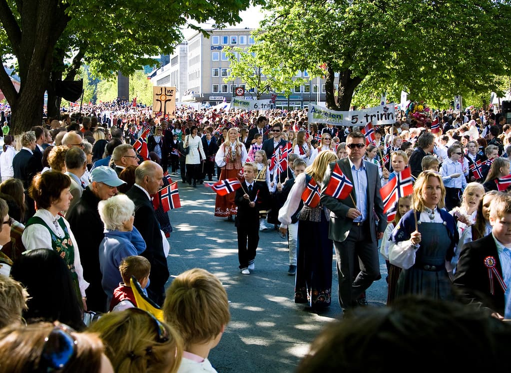 Crowds line a tree-lined street as a children's parade with Norwegian flags passes on May 17 in Trondheim