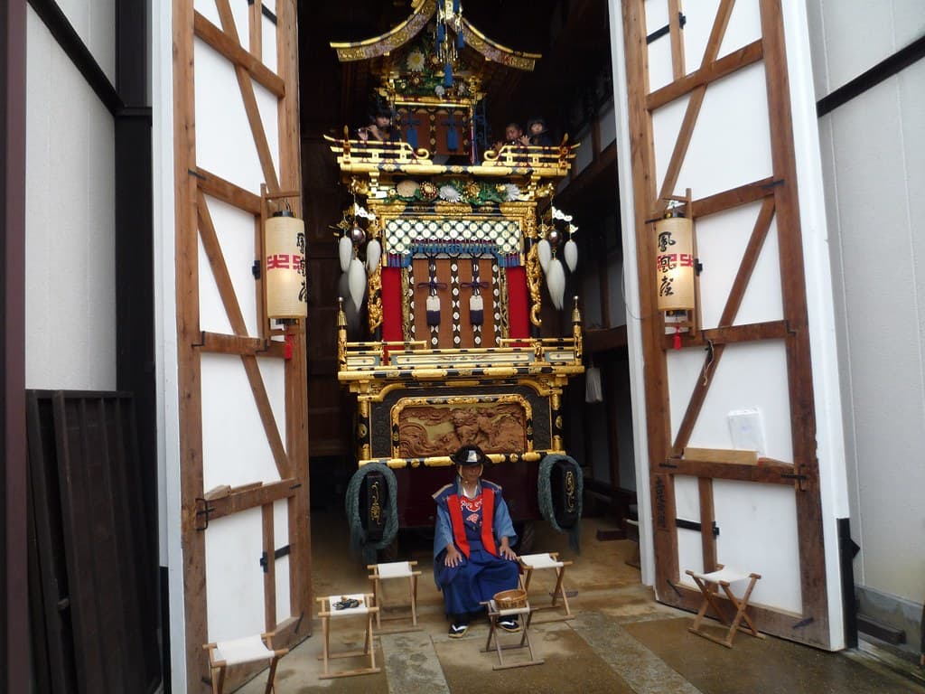An ornate gilded yatai float hung with lanterns stands in its open storehouse during the autumn Takayama Festival