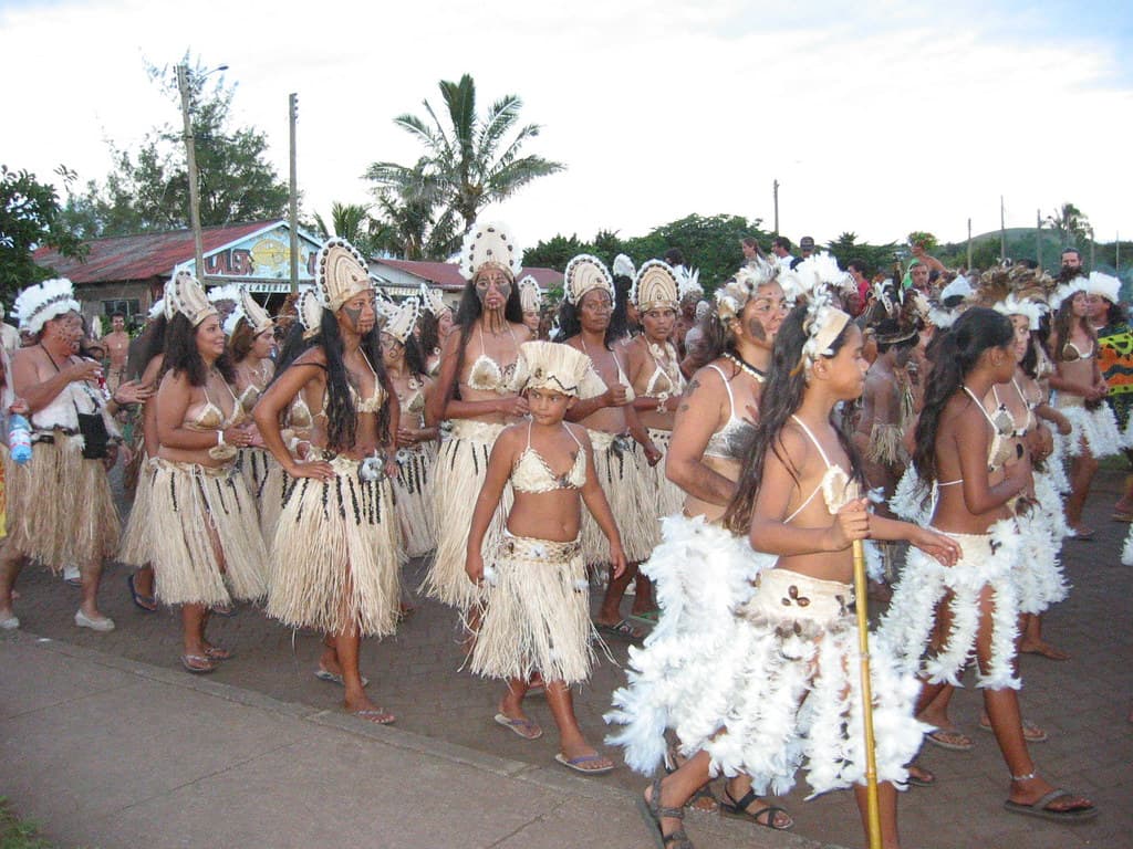Women in grass skirts and feathered headdresses dance in the street during the Tapati parade on Rapa Nui