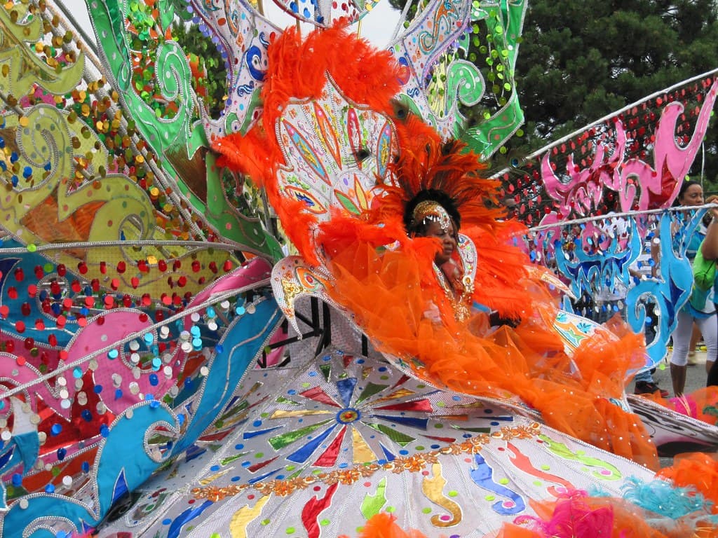 A masquerader in an enormous orange and white feathered costume dances during the Toronto Caribbean Carnival parade