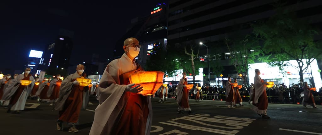A monk carrying a glowing lantern through Seoul during the Lotus Lantern Festival