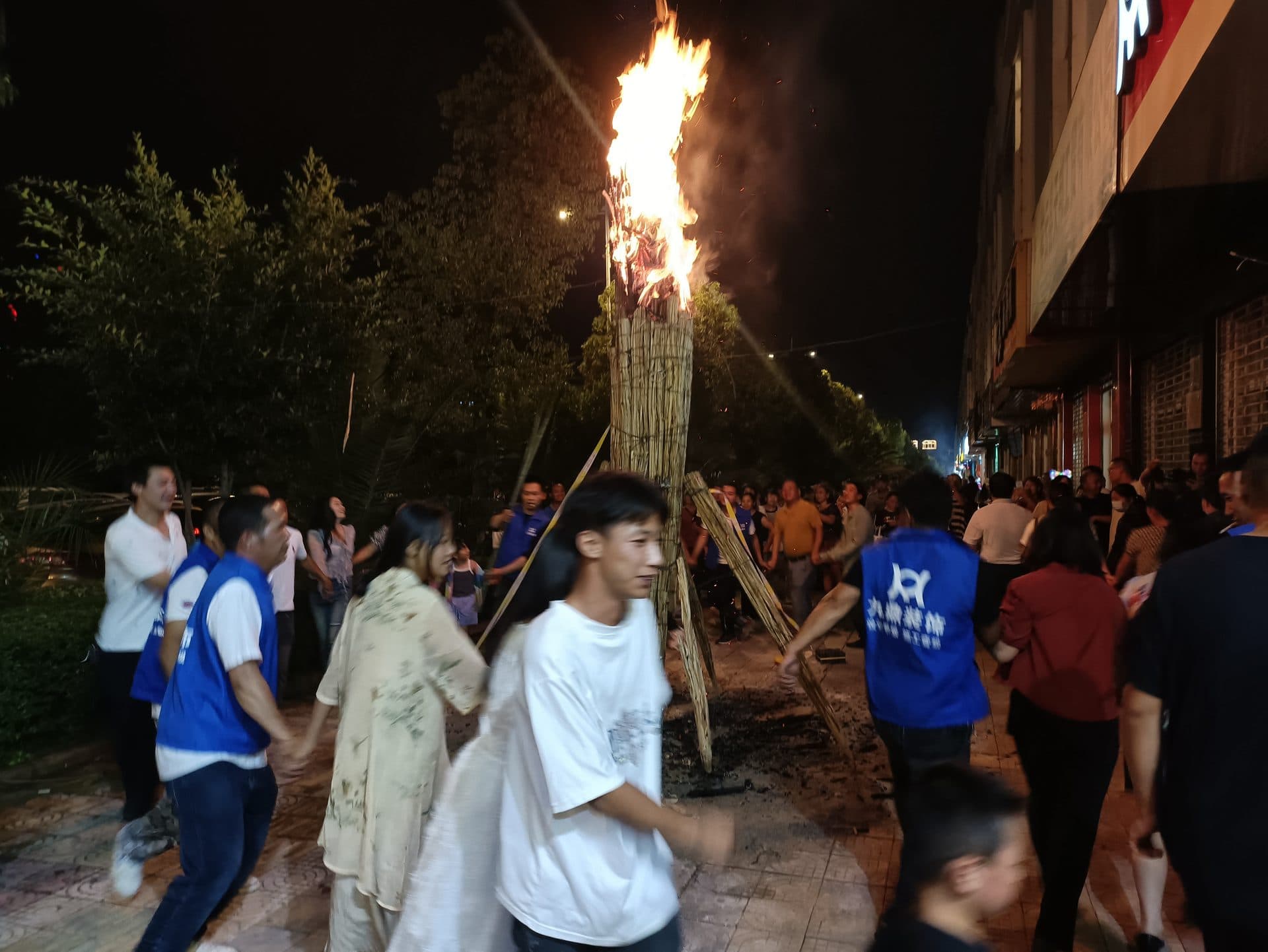 People gather around a blazing torch tower in a town square at night during the Torch Festival in Xiangyun, Yunnan