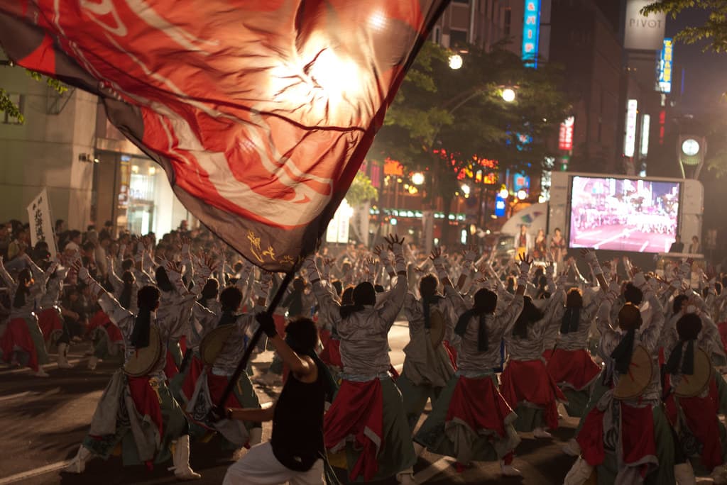 A huge red flag is waved over a dance team in red and white costumes at night during the YOSAKOI Soran Festival in Sapporo
