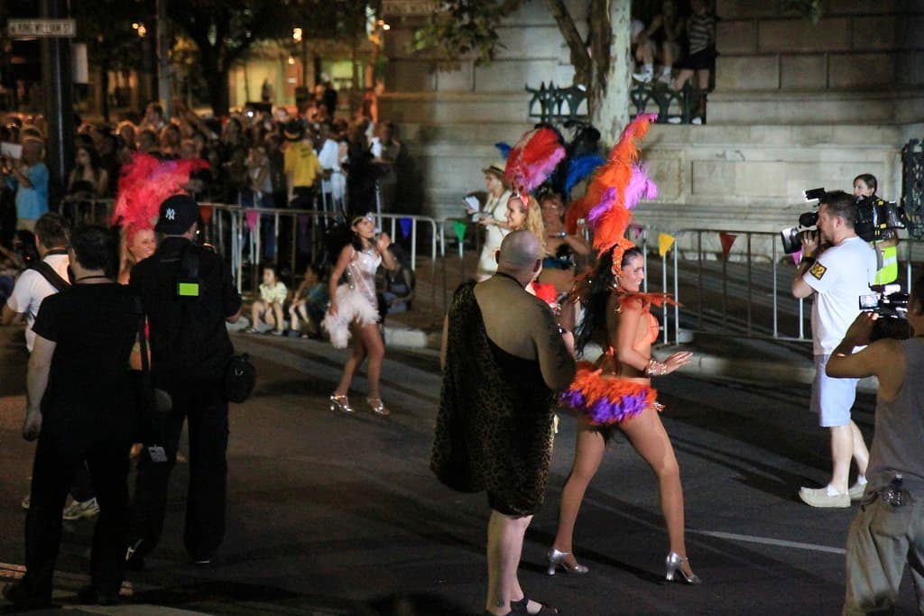 Performers in colourful feathered costumes dance in a city street at night during the Adelaide Fringe opening parade