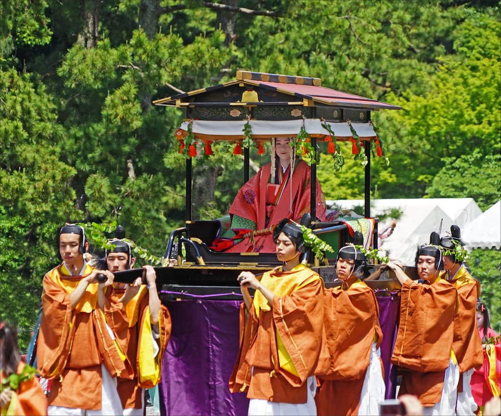 Attendants in orange robes accompany a black lacquered palanquin carrying the Saiō-dai in the Aoi Matsuri procession in Kyoto