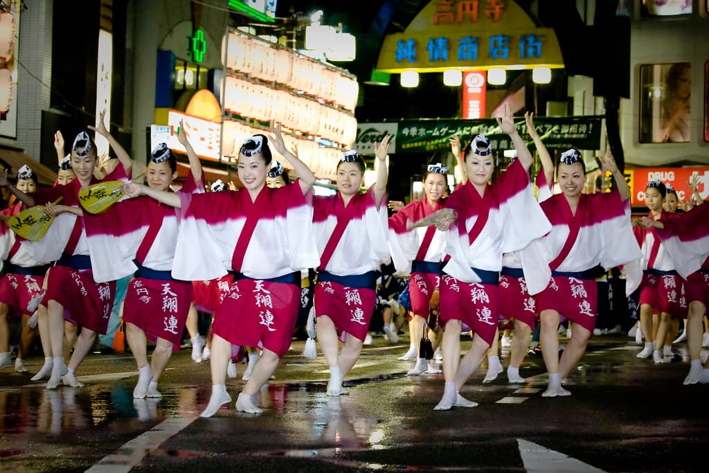 A line of Awa Odori dancers in pink and white costumes moving through a street