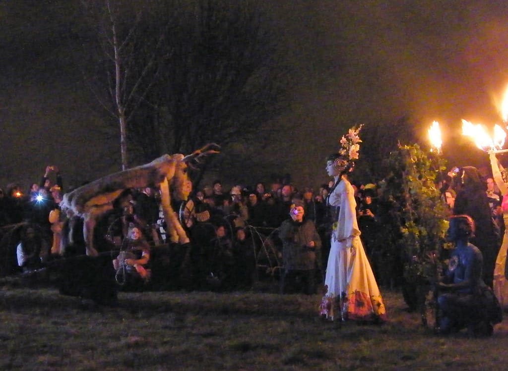 Performers costumed as a stag and the May Queen in white move across Calton Hill at night, watched by a crowd