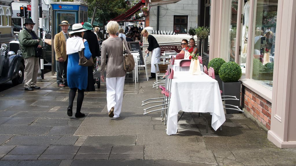 People in boaters and summer clothes stroll past tables set with white cloths outside a café in Dublin on Bloomsday
