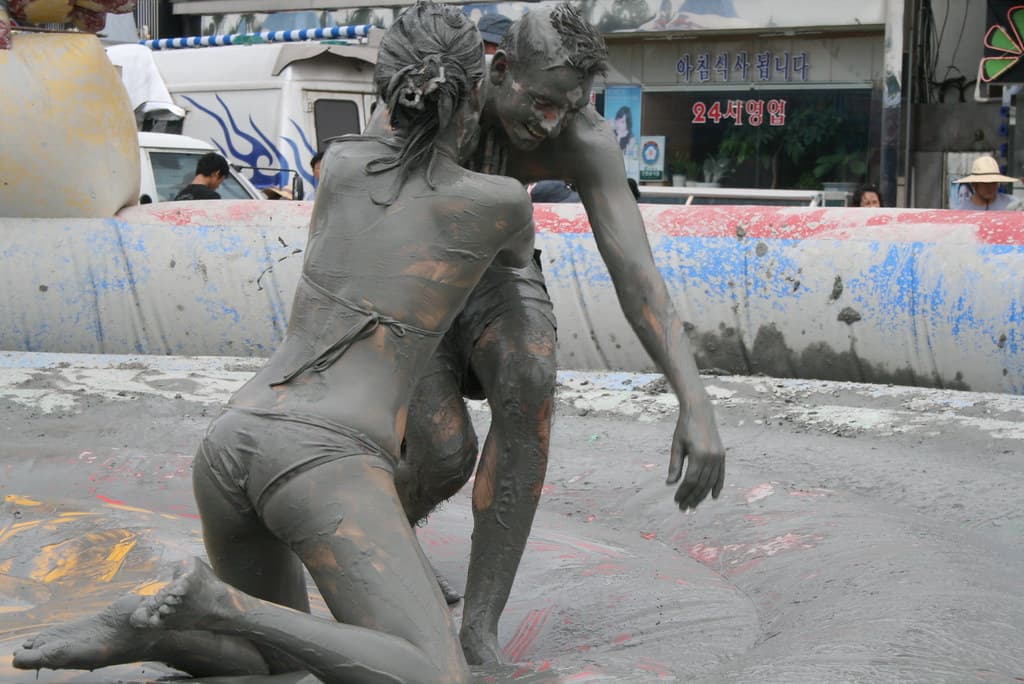 Two festival-goers covered in grey mud wrestle in a mud pit