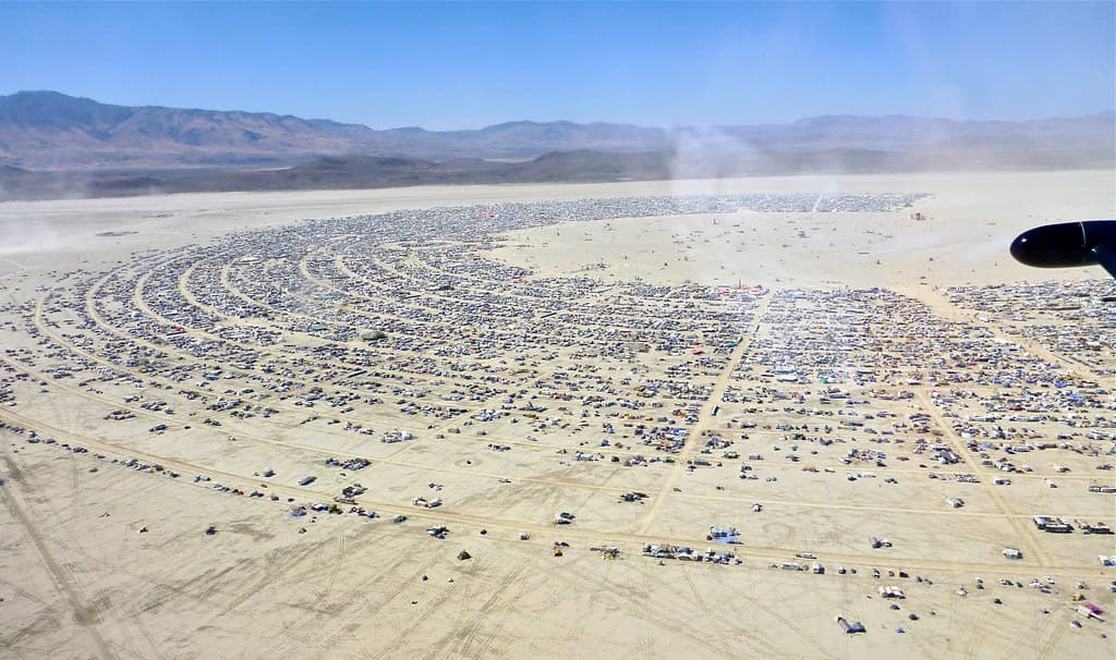 An aerial view of Black Rock City, a great arc of camps and streets spread across the pale dry lakebed of the Nevada desert