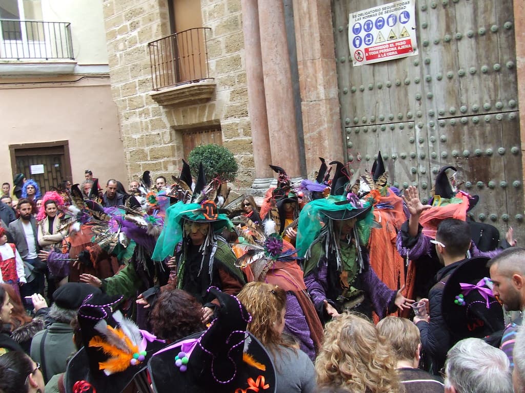 A crowd of carnival-goers in costumes and wigs fills a street in the old town of Cádiz