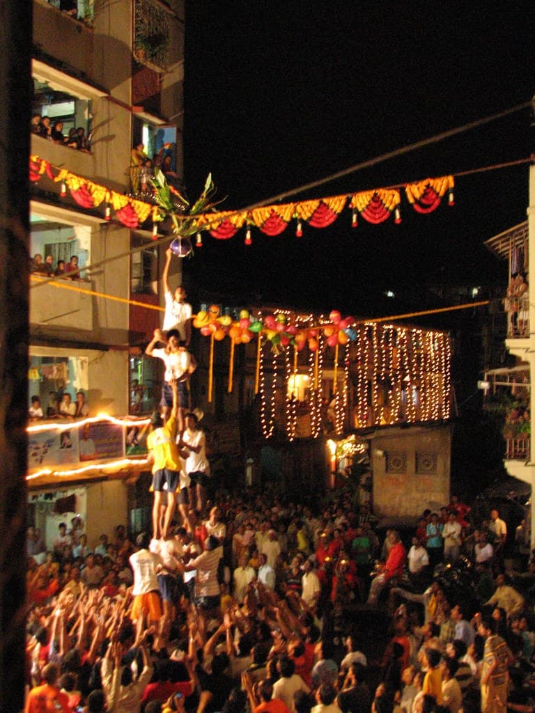 At night, Govinda climbers form a pyramid under festival lights in a packed street in Girgaum, Mumbai