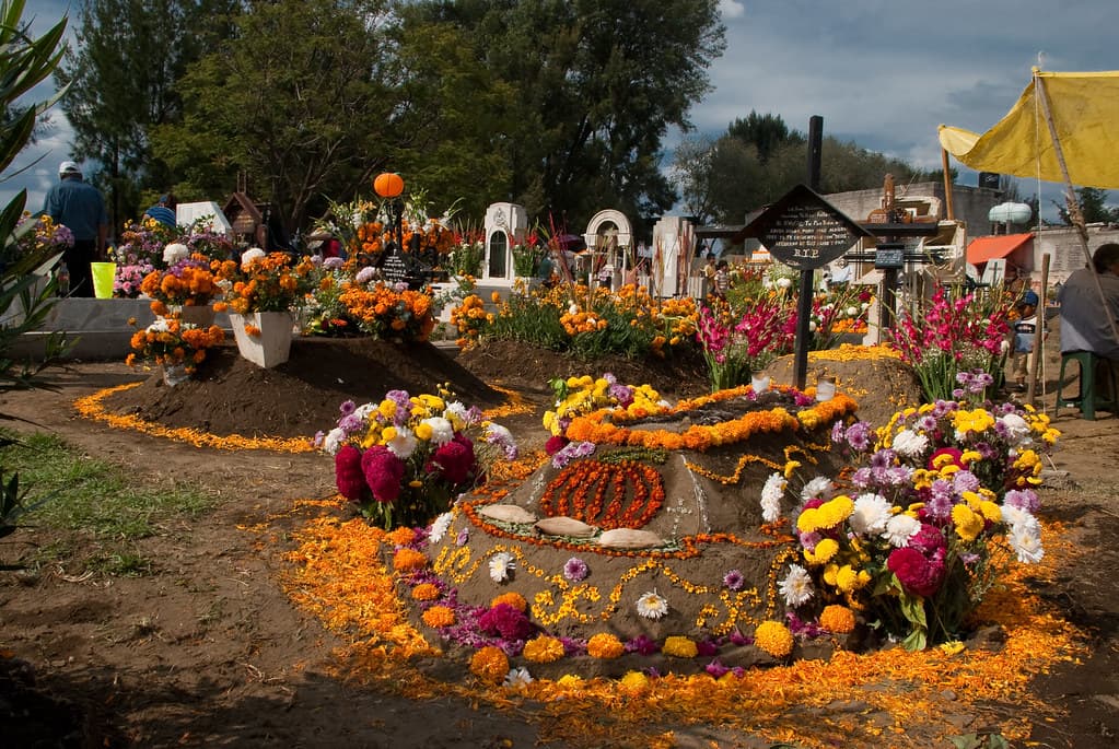 A grave mounded with earth and outlined in orange marigold petals and flowers in a village cemetery