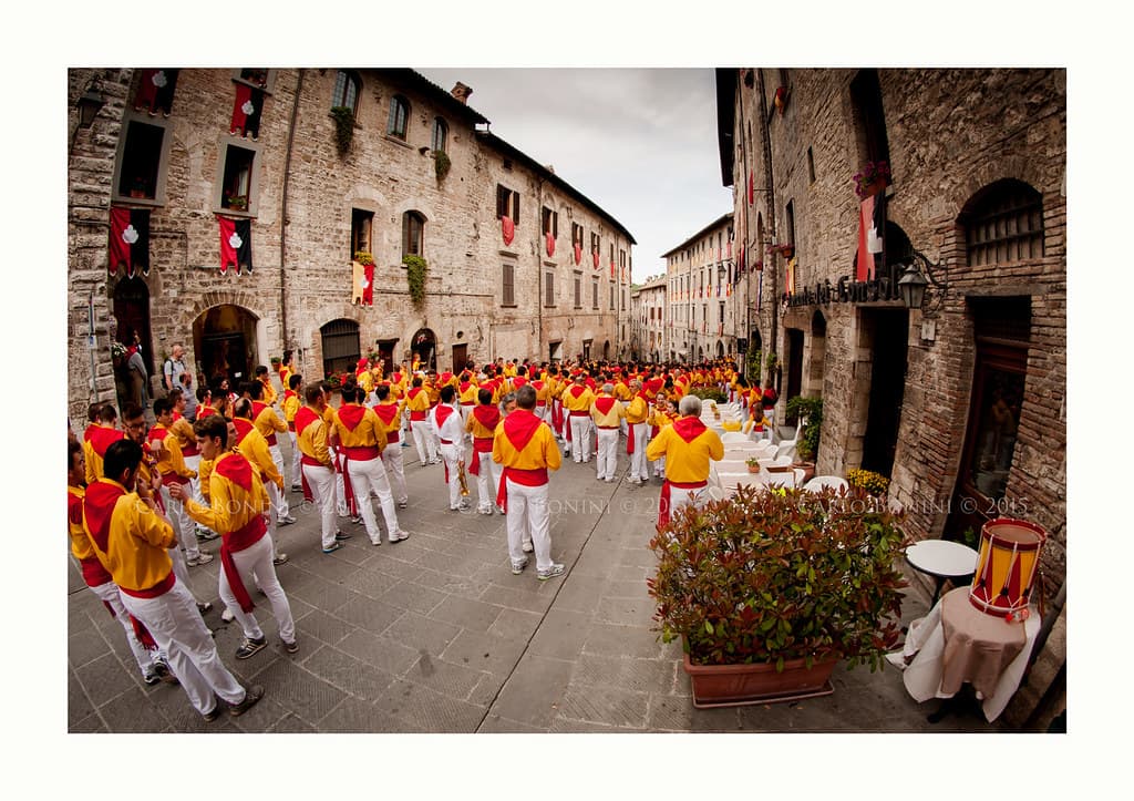 A team of ceraioli in yellow shirts and red sashes fills a stone street in Gubbio