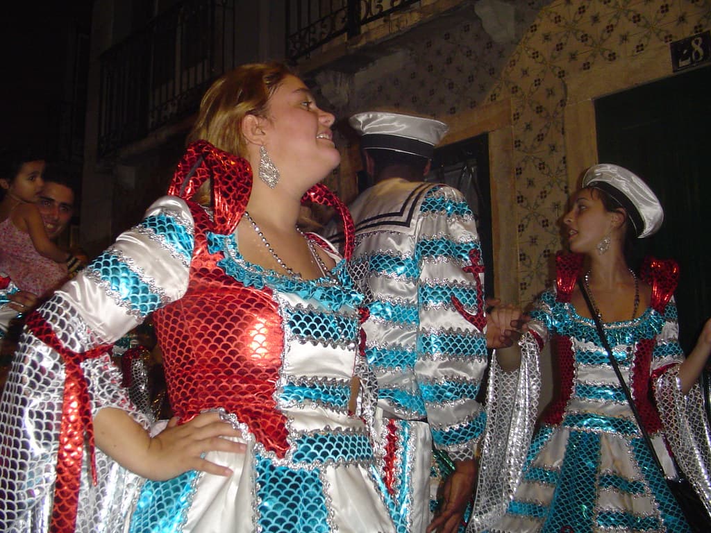 Marchers in sequinned costumes in blue, white and red pose in a narrow Lisbon street before the Marchas Populares