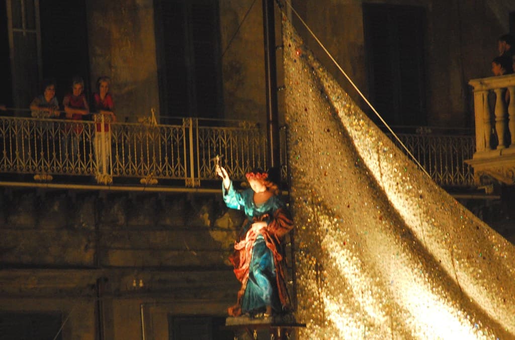 A statue of Saint Rosalia in a blue robe beneath a glittering gold canopy during the Festino in Palermo