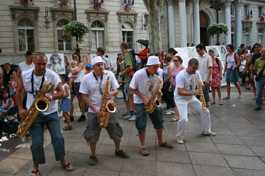 A brass band in white plays saxophones and trombones in a square in Avignon during the festival