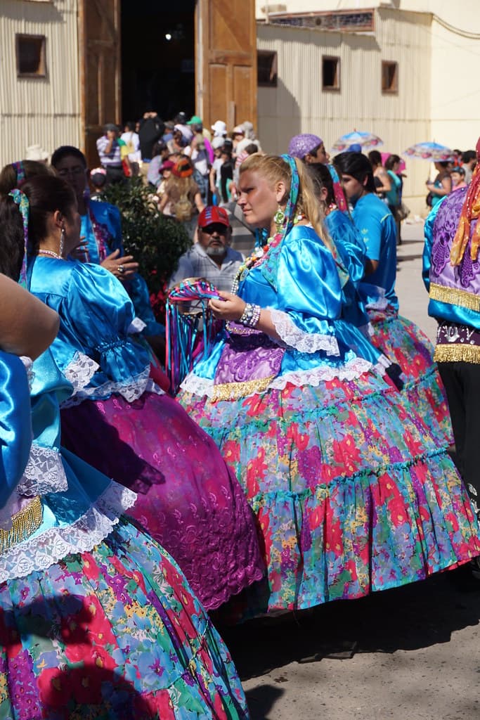 Dancers in bright blue and pink costumes rest in front of the sanctuary during the Fiesta de La Tirana