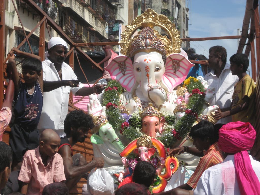 A large pink and gold Ganesh idol, garlanded with flowers, is carried through a Mumbai street by a crowd of men