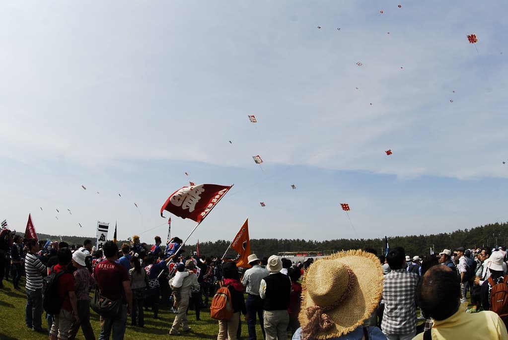 Teams with banners fly kites over a grassy field at Nakatajima during the Hamamatsu Matsuri