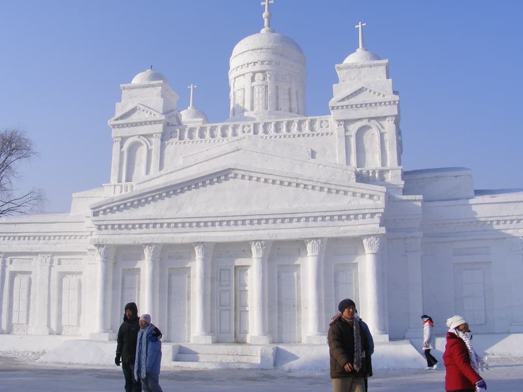A church sculpted from snow, with visitors in winter coats walking past, at the Harbin International Ice and Snow Sculpture Festival