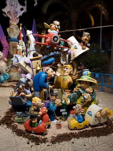 A colourful hoguera monument of cartoon figures, cars and planes stands in an Alicante street at night