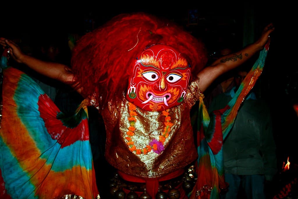 A masked Majipa Lakhey dancer with a red demon face, a mane of red hair and colourful flowing sleeves performs at night