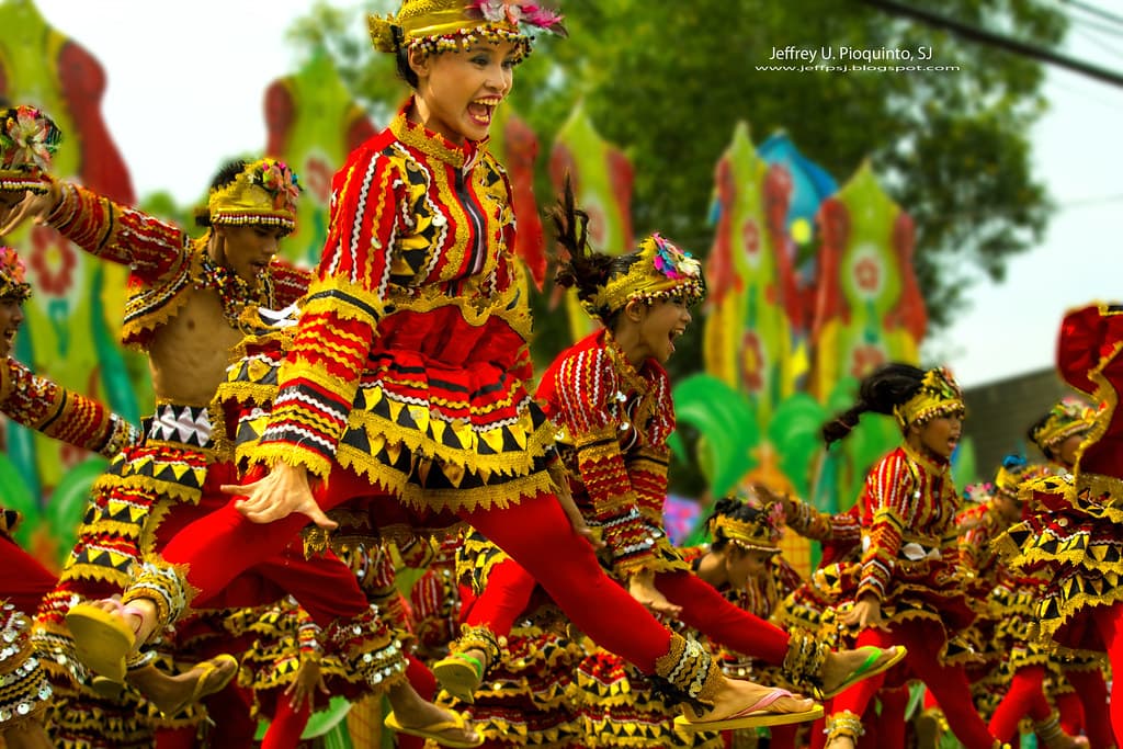 Dancers in red and gold costumes with feathered headpieces leap during a street parade