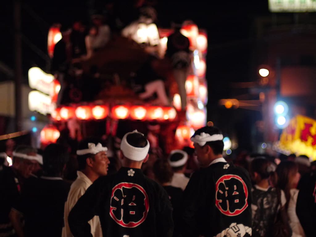 A danjiri float hung with glowing lanterns is pulled through Kishiwada at night by men in matching happi coats