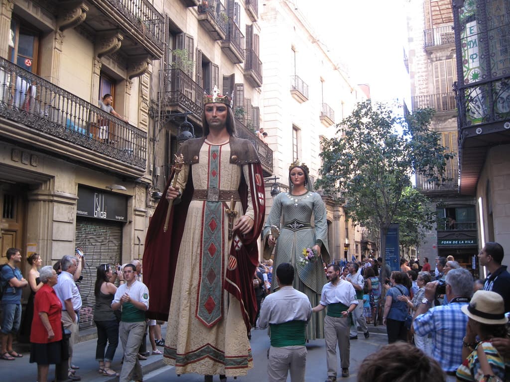 Two tall robed giants, a king and a queen, dance in a narrow street in Barcelona's old town, surrounded by onlookers