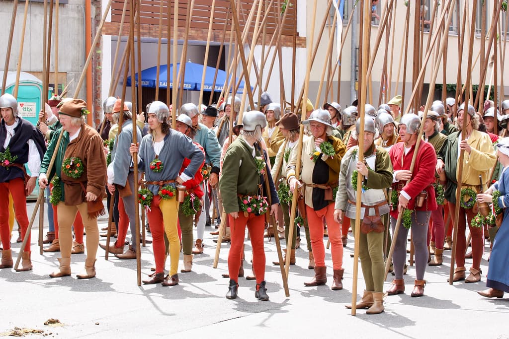 Rows of costumed foot soldiers with long pikes and medieval clothing assemble in a Landshut street for the wedding procession