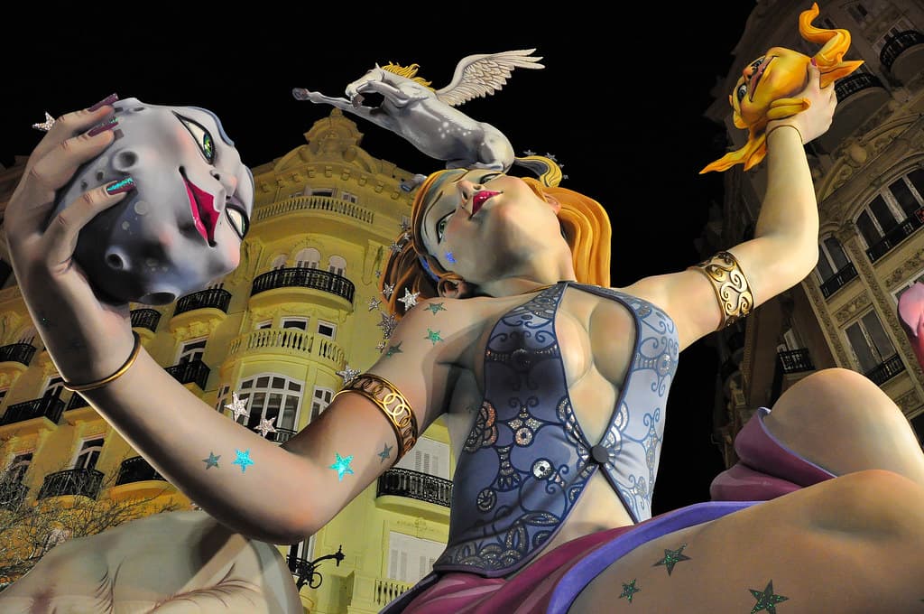 An ornate falla sculpture of a figure with raised arms against the night sky