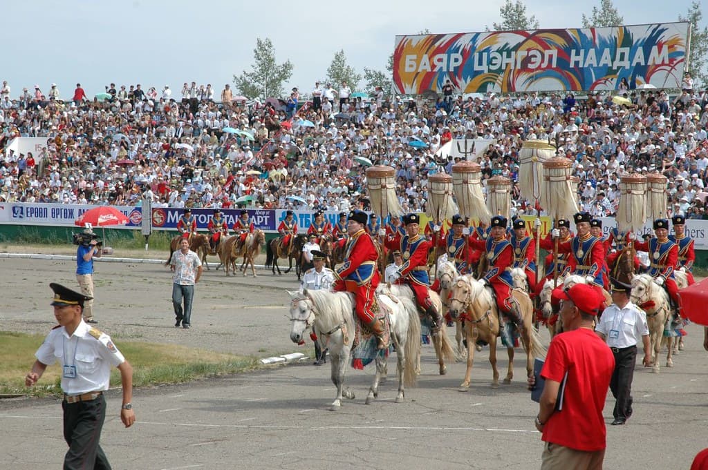 Horses and riders parading in front of the stands at a Naadam opening ceremony