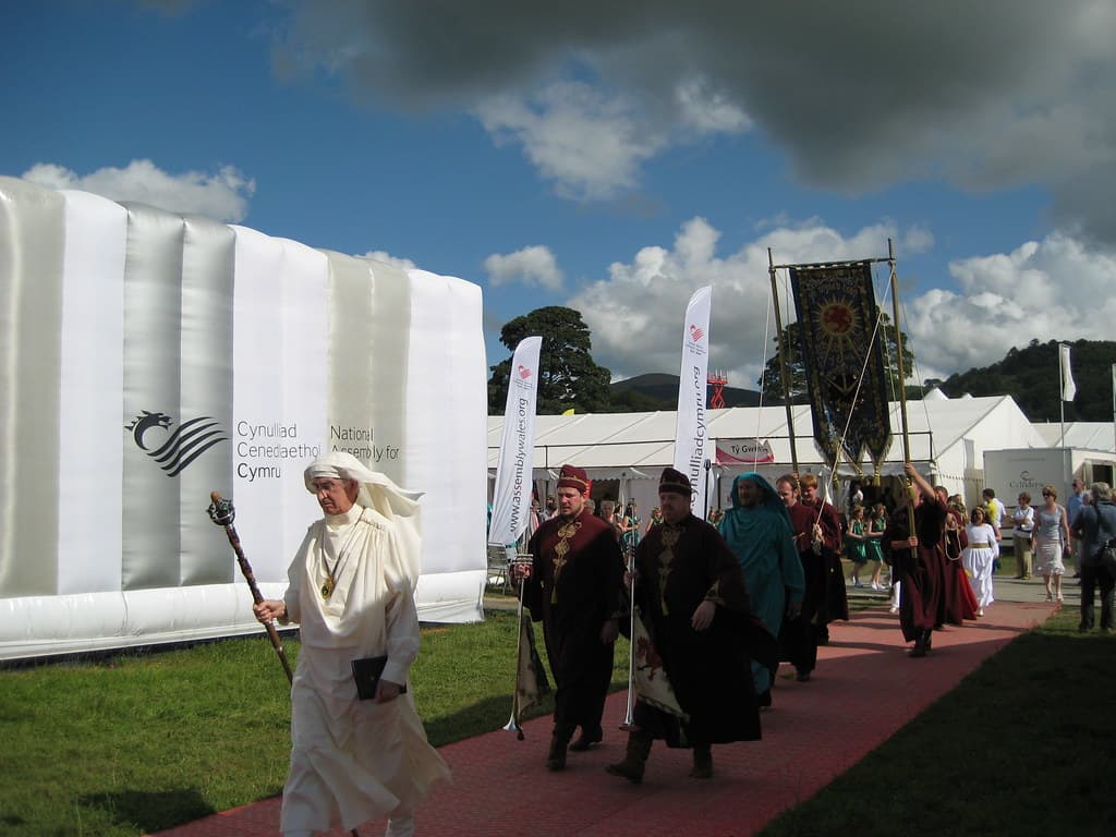 Robed members of the Gorsedd walk past white pavilions on the Maes at the National Eisteddfod of Wales