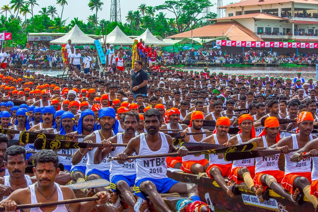 Rows of rowers in matching vests and caps sit in a long snake boat on Punnamada Lake before the finals