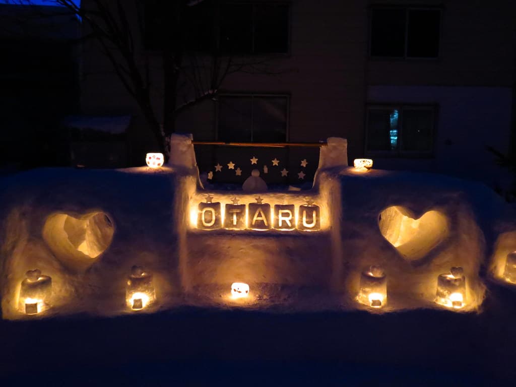 Candles glow in snow sculptures shaped like hearts and the word Otaru along a snowy path at night