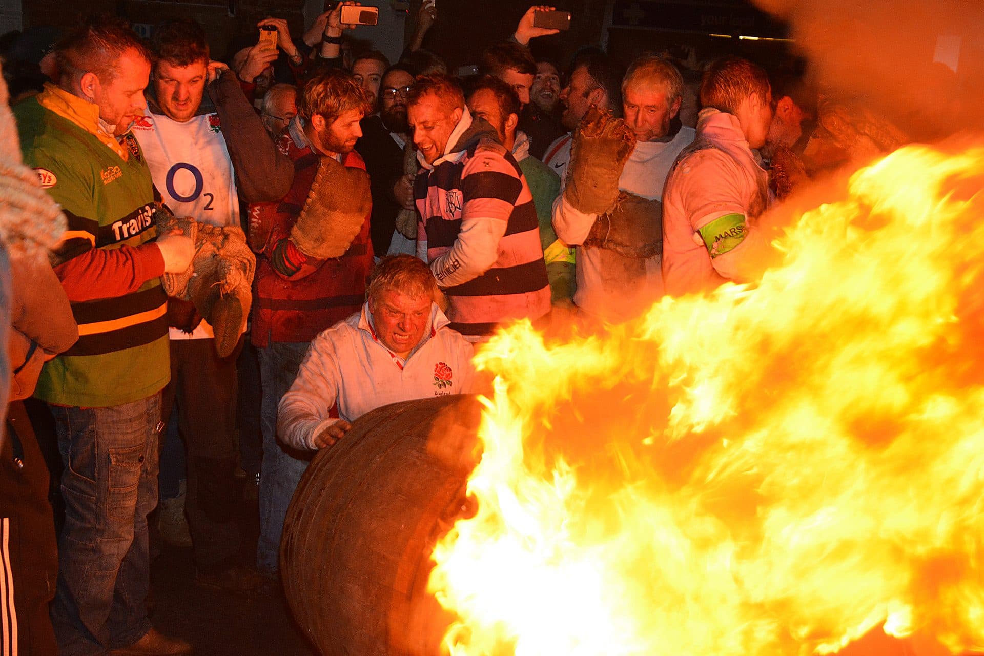 A burning tar barrel carried through a tightly packed crowd in Ottery St Mary