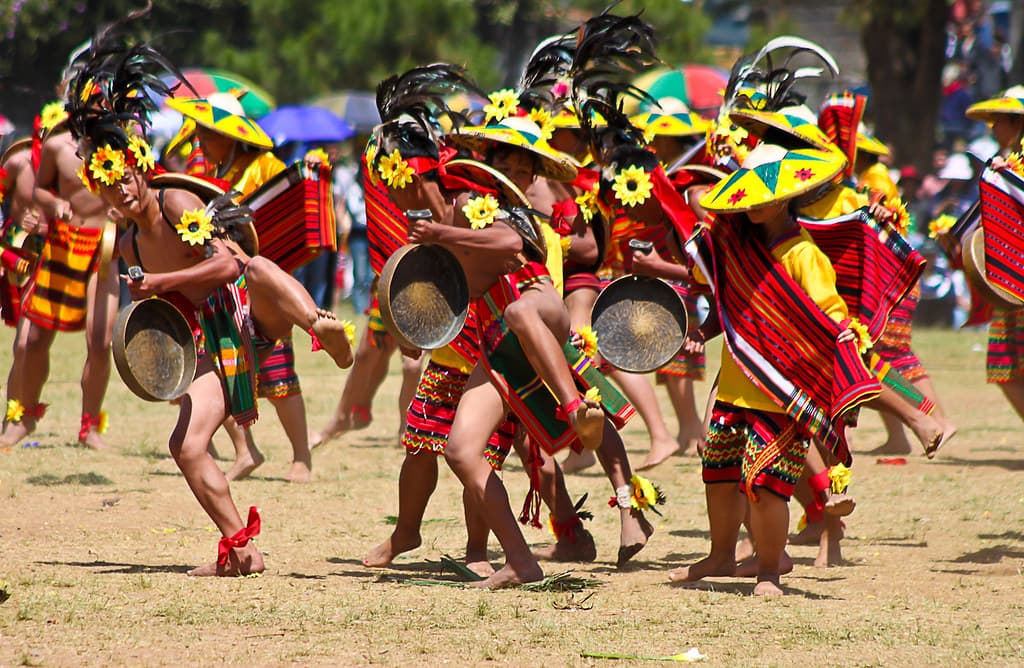 Street dancers in red and yellow costumes with painted shields perform on a field in Baguio