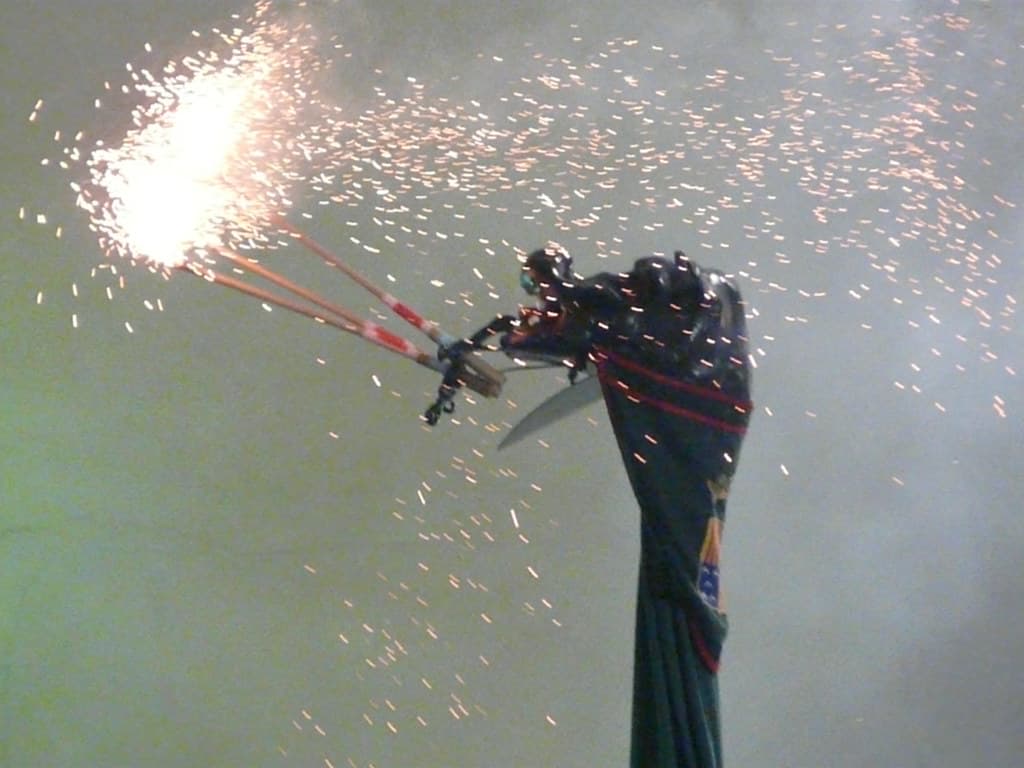 A dark costumed figure with a long neck spits a shower of sparks from fireworks into the smoky air during La Patum de Berga