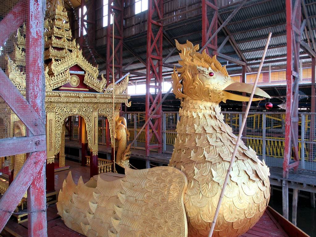A gilded royal barge shaped like a bird, housed in a shed beside the water