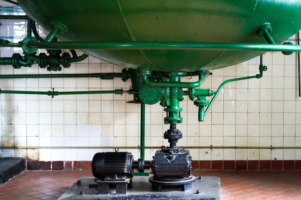 A large historic green brewing tank with pipes and valves stands in a white-tiled room at the Tsingtao Beer Museum