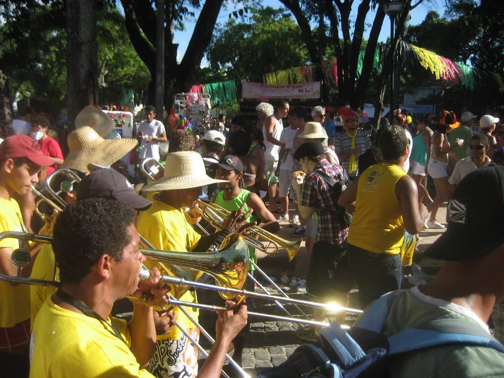 A frevo brass band in yellow shirts plays trombones in a crowded square in Olinda during carnival