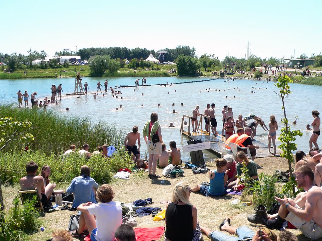 Festival-goers swim and sunbathe at a lake on the edge of the Roskilde Festival campsite under a clear blue sky