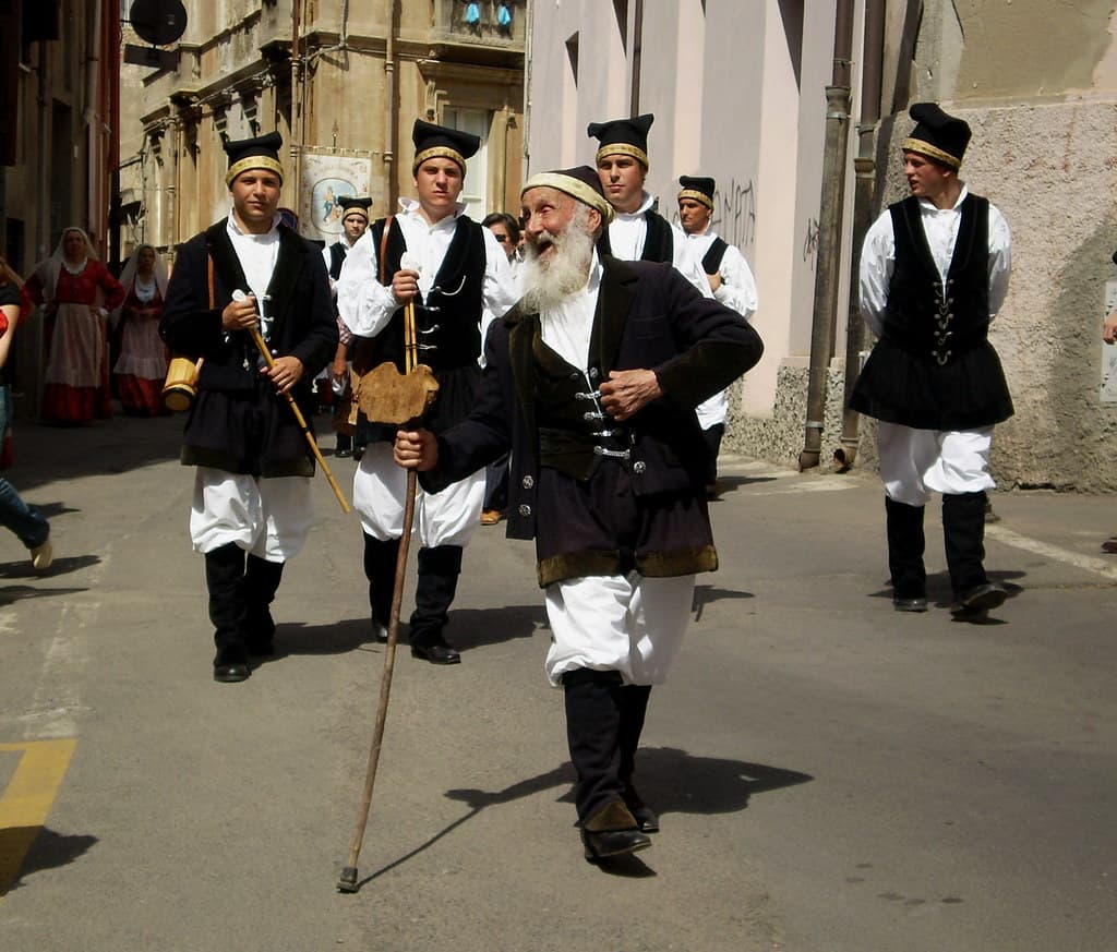 Men in traditional black and white Sardinian dress walk with a cane in the Sant'Efisio procession through the streets of Cagliari
